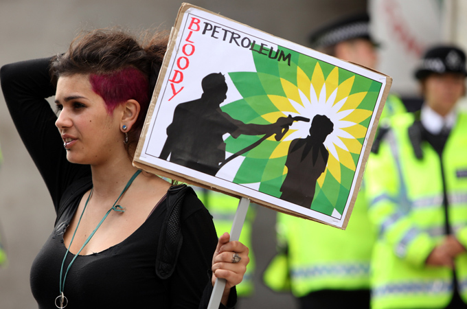 A woman holding a placard sign saying "Bloody Petroleum"